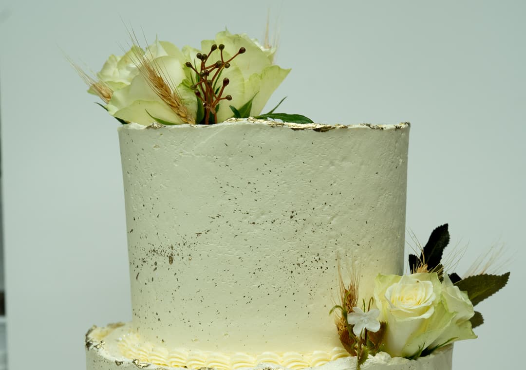 Close-up of an elegant celebration cake with gold leaf and white roses