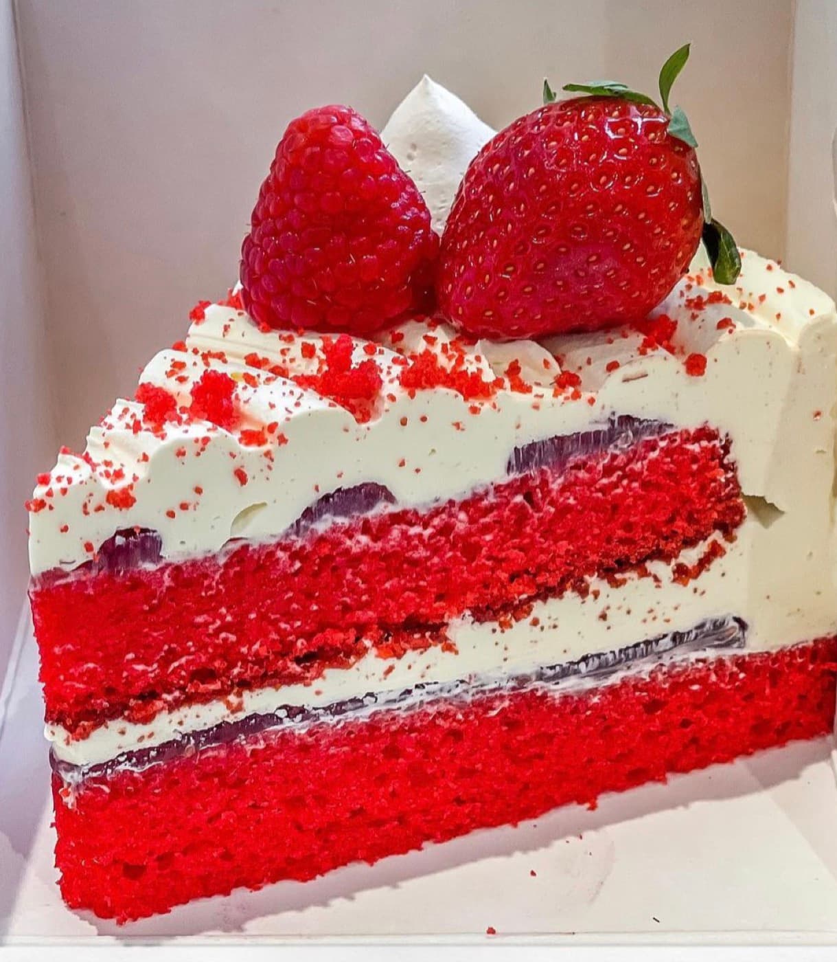 Slice of layered red cake with cream and fresh strawberries
